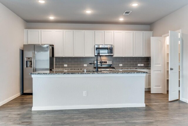 2089 Hartley Dr, Forney, TX 75126 - kitchen with appliances with stainless steel finishes, dark stone counters, an island with sink, white cabinets, and decorative backsplash