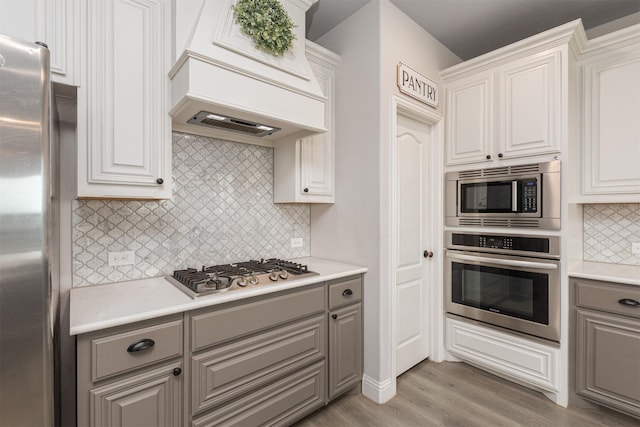 2014 Slow Stream Dr, Royse City, TX 75189 - kitchen with stainless steel appliances, gray cabinetry, premium range hood, backsplash, and light wood finished floors