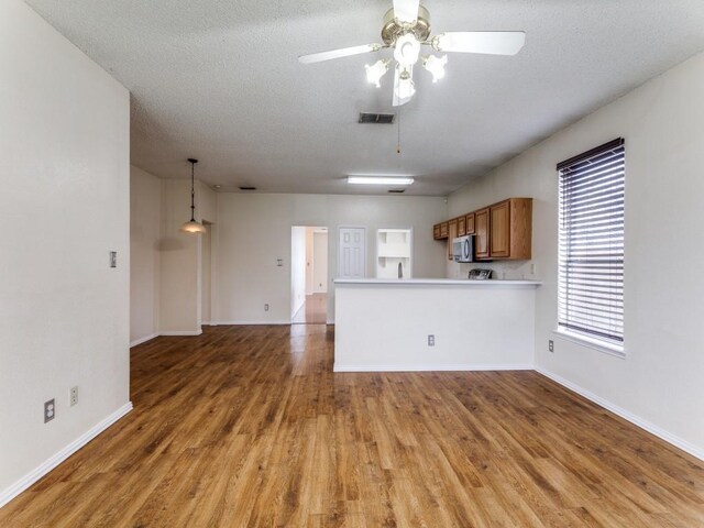 7116 Park Creek Cir E, Fort Worth, TX 76137 - kitchen with brown cabinets, light wood finished floors, stainless steel microwave, light countertops, and baseboards