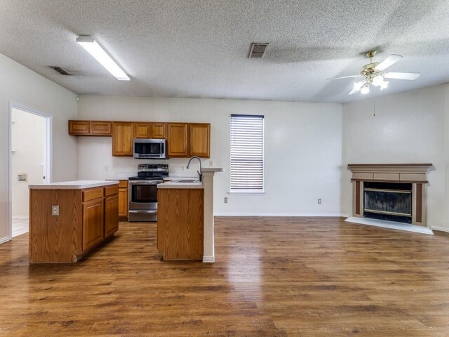7116 Park Creek Cir E, Fort Worth, TX 76137 - kitchen featuring appliances with stainless steel finishes, brown cabinetry, open floor plan, dark wood finished floors, and a ceiling fan