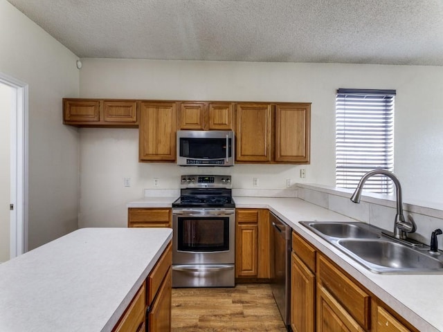 7116 Park Creek Cir E, Fort Worth, TX 76137 - kitchen with stainless steel appliances, a sink, brown cabinetry, a textured ceiling, and light countertops