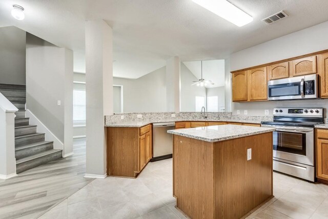 9736 Old Field Dr, Mckinney, TX 75072 - kitchen with appliances with stainless steel finishes, a sink, a center island, light stone countertops, and brown cabinetry