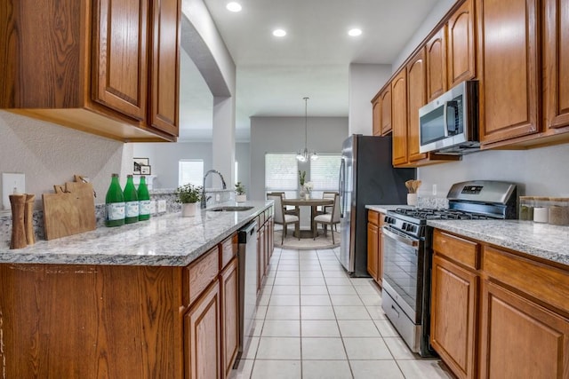 9405 Log Run Ct, Mckinney, TX 75072 - kitchen with stainless steel appliances, a sink, brown cabinetry, light stone counters, and light tile patterned floors