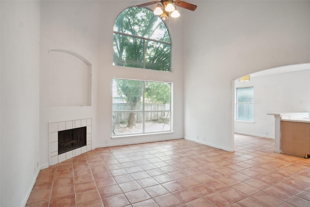 317 Stately Oak Ln, Lake Dallas, TX 75065 - unfurnished living room featuring a towering ceiling, arched walkways, a tile fireplace, ceiling fan, and baseboards