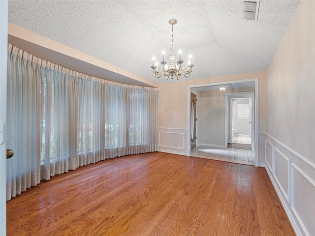 211 Indian Trace Ln, Waxahachie, TX 75165 - unfurnished room with a chandelier, a decorative wall, wood finished floors, lofted ceiling, and a textured ceiling