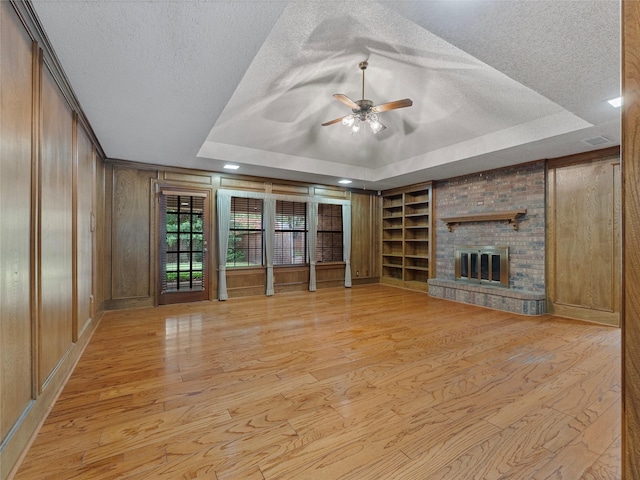 211 Indian Trace Ln, Waxahachie, TX 75165 - unfurnished living room with a raised ceiling, light wood-type flooring, a textured ceiling, ceiling fan, and a brick fireplace