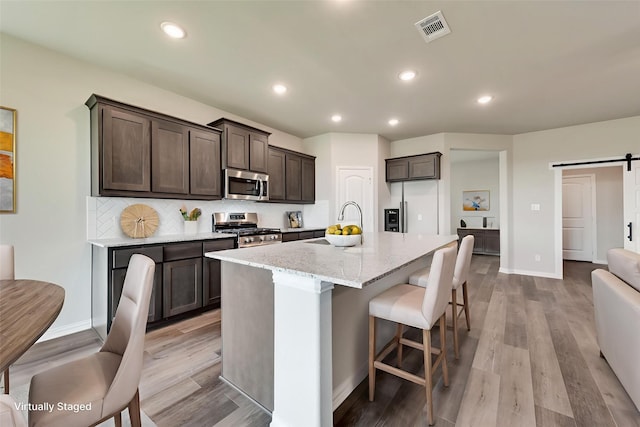 616 Juneau St, Gainesville, TX 76240 - kitchen featuring stainless steel appliances, a barn door, dark brown cabinetry, light wood-style flooring, and recessed lighting