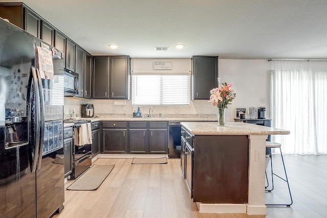 2604 Norite Dr, Fort Worth, TX 76108 - kitchen with black appliances, a sink, light wood finished floors, a kitchen island, and a breakfast bar
