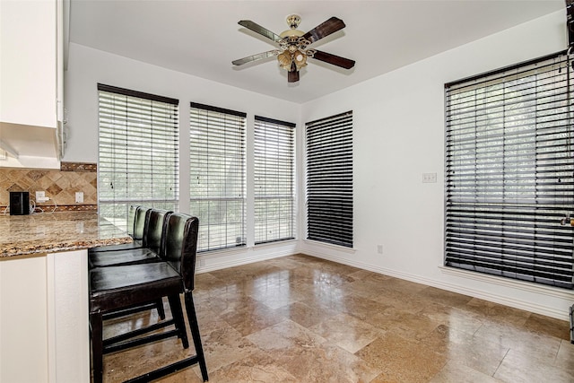 3308 Corn Valley Rd, Grand Prairie, TX 75052 - kitchen featuring ceiling fan, white cabinetry, decorative backsplash, a kitchen bar, and light stone countertops