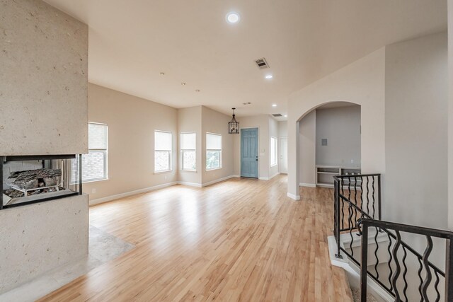 11 Intrepid Cir, Rockwall, TX 75032 - unfurnished living room with arched walkways, light wood finished floors, baseboards, recessed lighting, and a multi sided fireplace