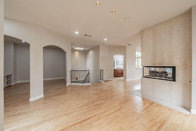 11 Intrepid Cir, Rockwall, TX 75032 - unfurnished living room featuring arched walkways, light wood-type flooring, recessed lighting, a multi sided fireplace, and baseboards