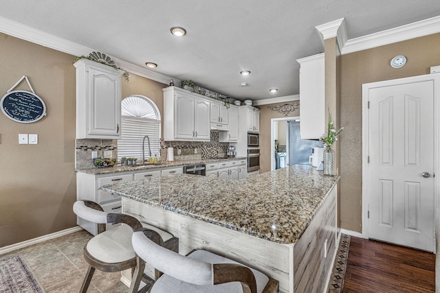 2829 Flint Rock Dr, Fort Worth, TX 76131 - kitchen featuring a sink, crown molding, baseboards, a kitchen bar, and white cabinetry