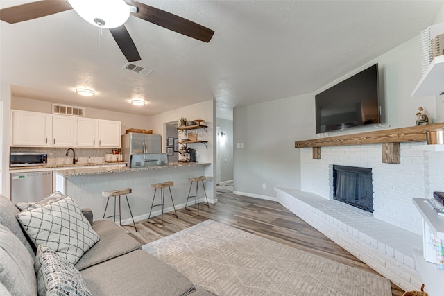 6117 Magnolia Ln, Rowlett, TX 75089 - living area featuring light wood-style floors, ceiling fan, baseboards, and a brick fireplace