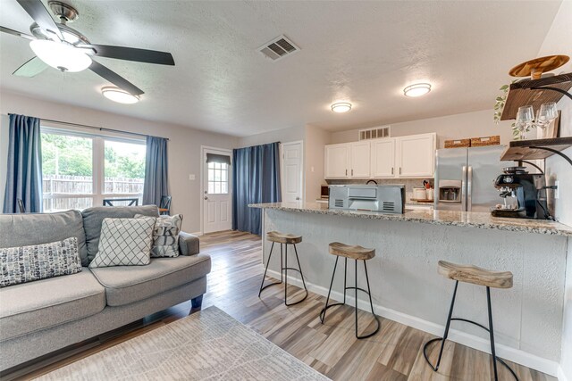 6117 Magnolia Ln, Rowlett, TX 75089 - kitchen with stainless steel fridge, a breakfast bar, white cabinets, light wood finished floors, and light stone counters