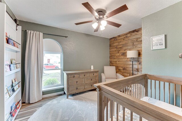 6117 Magnolia Ln, Rowlett, TX 75089 - bedroom with a textured wall, wood walls, ceiling fan, and a crib
