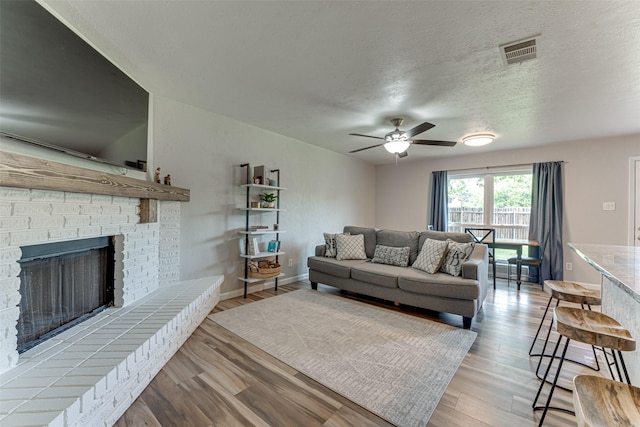 6117 Magnolia Ln, Rowlett, TX 75089 - living area featuring a ceiling fan, wood finished floors, a brick fireplace, a textured ceiling, and baseboards