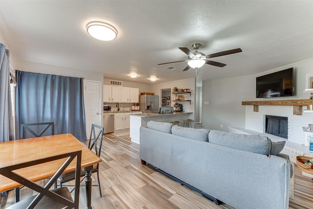 6117 Magnolia Ln, Rowlett, TX 75089 - living area featuring light wood-style flooring, a ceiling fan, and a brick fireplace