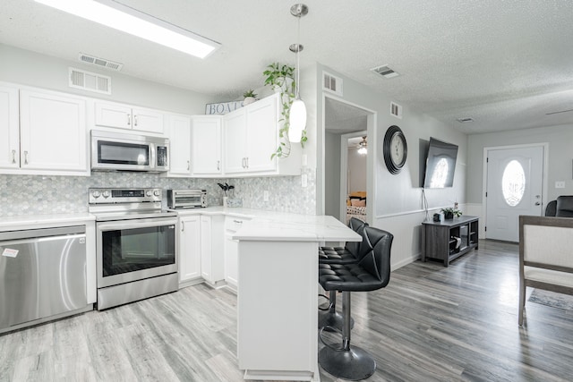 1100 Cartwright Ln, Kaufman, TX 75142 - kitchen with appliances with stainless steel finishes, a kitchen breakfast bar, light wood-style flooring, white cabinetry, and a textured ceiling