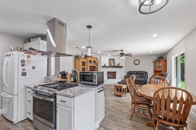 3005 Hillcrest Dr, Corsicana, TX 75110 - kitchen with gas stove, island exhaust hood, a ceiling fan, white cabinets, and a brick fireplace