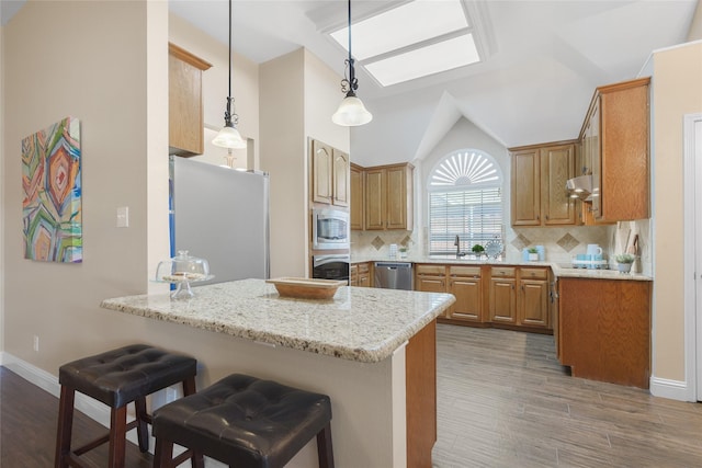 10105 Hunter Run, Frisco, TX 75035 - kitchen with appliances with stainless steel finishes, a peninsula, a kitchen breakfast bar, wood finished floors, and lofted ceiling