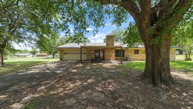 1015 Monte Carlo Dr, Grand Saline, TX 75140 - ranch-style house with driveway, an attached garage, a chimney, cooling unit, and metal roof