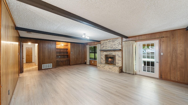 1015 Monte Carlo Dr, Grand Saline, TX 75140 - unfurnished living room with wooden walls, beamed ceiling, a textured ceiling, light wood finished floors, and a fireplace