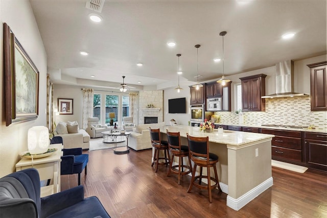 917 Navasota Trl, Mckinney, TX 75071 - kitchen with open floor plan, wall chimney exhaust hood, a ceiling fan, a fireplace, and a kitchen bar