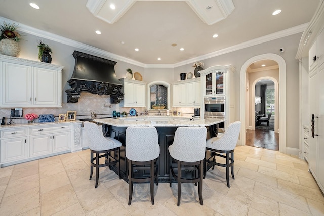 504 Bristol Dr, Allen, TX 75013 - kitchen with premium range hood, stone tile flooring, arched walkways, an island with sink, and a breakfast bar area