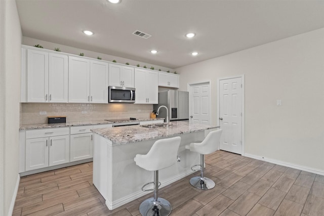 620 Ruthye Ln, Pilot Point, TX 76258 - kitchen featuring stainless steel appliances, a sink, a kitchen island with sink, light wood-type flooring, and white cabinets