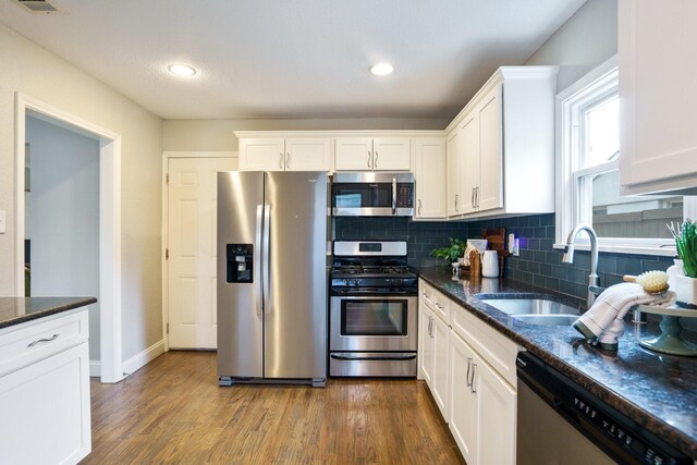 4731 Wateka Dr, Dallas, TX 75209 - kitchen featuring appliances with stainless steel finishes, a sink, white cabinets, wood finished floors, and tasteful backsplash