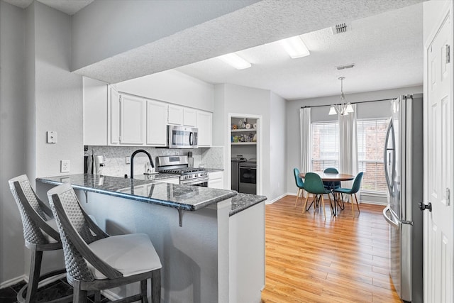 736 Fawn Valley Dr, Allen, TX 75002 - kitchen featuring appliances with stainless steel finishes, a peninsula, light wood-type flooring, a kitchen breakfast bar, and white cabinetry