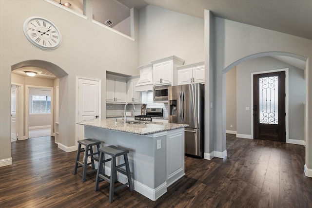 1108 Summer Ln, Mckinney, TX 75071 - kitchen featuring appliances with stainless steel finishes, arched walkways, light stone counters, an island with sink, and white cabinetry