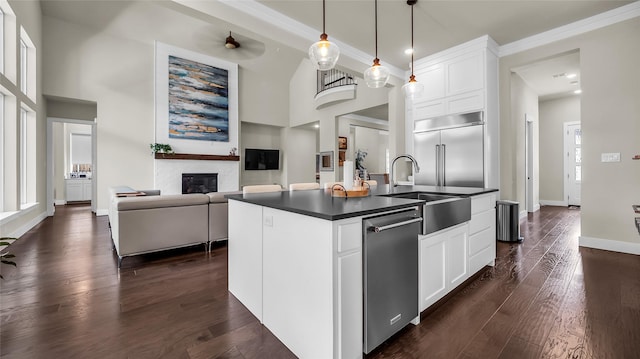 8162 Edgefield Ct, Frisco, TX 75035 - kitchen with appliances with stainless steel finishes, dark countertops, a glass covered fireplace, an island with sink, and white cabinets
