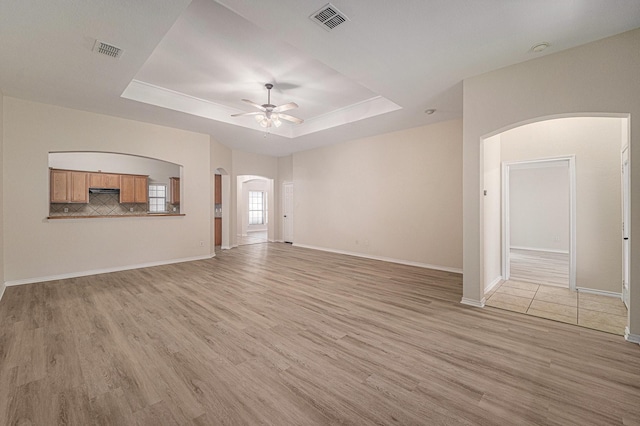 5516 La Bandera Trl, Benbrook, TX 76126 - unfurnished living room featuring arched walkways, a ceiling fan, light wood-style floors, a tray ceiling, and baseboards