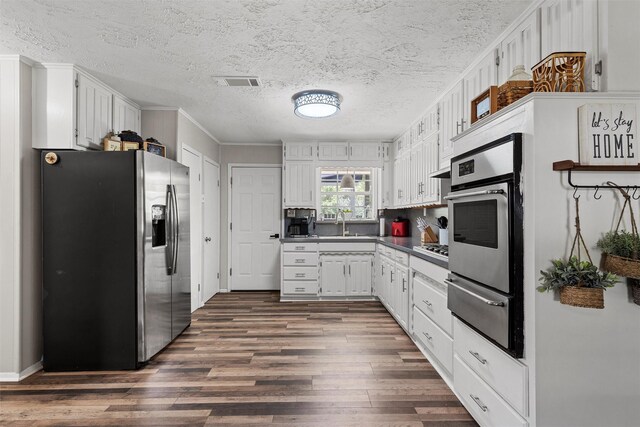 102 Creek Dr, Whitney, TX 76692 - kitchen with appliances with stainless steel finishes, a warming drawer, dark wood-style floors, dark countertops, and white cabinets
