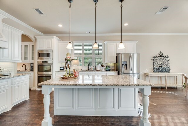 901 Jessica Ln, Prosper, TX 75078 - kitchen featuring appliances with stainless steel finishes, a breakfast bar area, white cabinetry, ornamental molding, and a center island