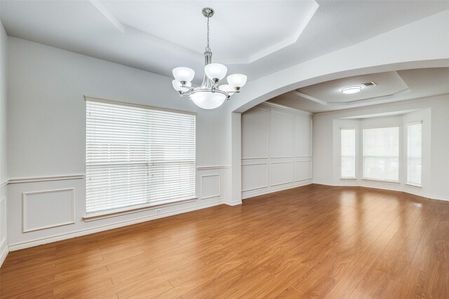 5283 W Cove Way, Grand Prairie, TX 75052 - empty room with a tray ceiling, a chandelier, light wood-style floors, arched walkways, and a decorative wall