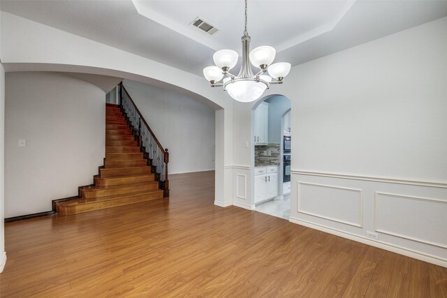 5283 W Cove Way, Grand Prairie, TX 75052 - unfurnished dining area with light wood-style floors, a raised ceiling, a chandelier, arched walkways, and stairway