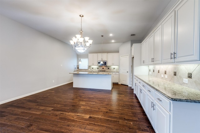 9728 Bitterroot Dr, Little Elm, TX 75068 - kitchen featuring a chandelier, tasteful backsplash, stainless steel microwave, a center island with sink, and white cabinetry