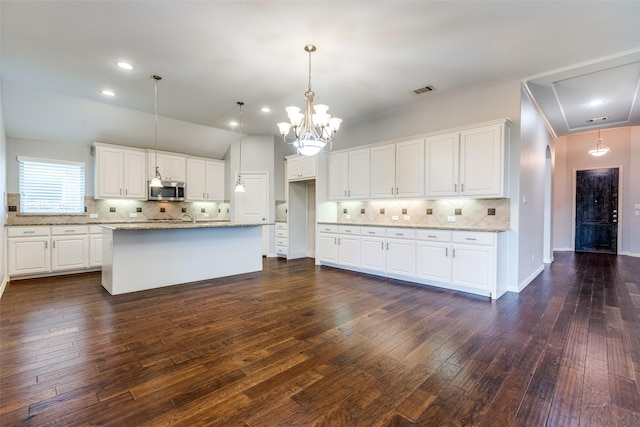 9728 Bitterroot Dr, Little Elm, TX 75068 - kitchen with stainless steel microwave, tasteful backsplash, dark wood-style flooring, light stone counters, and white cabinetry
