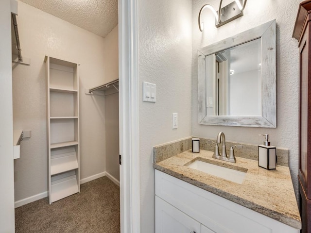 1603 Marsh Ln Unit 308, Carrollton, TX 75006 - bathroom with vanity, a textured ceiling, a spacious closet, baseboards, and a textured wall