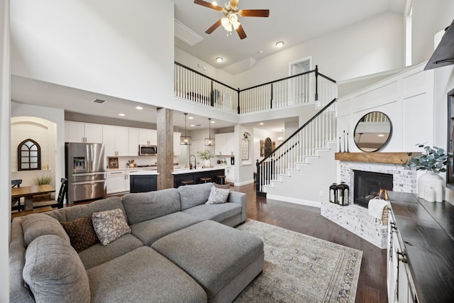 7717 Lake Worth Cv, Mckinney, TX 75071 - living room with a ceiling fan, dark wood-type flooring, a high ceiling, a brick fireplace, and stairway