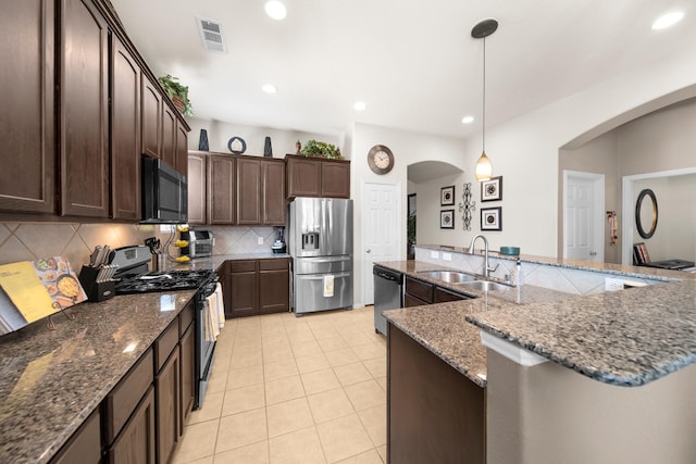 334 Hawthorn Dr, Fate, TX 75087 - kitchen featuring stainless steel appliances, a sink, arched walkways, dark brown cabinets, and decorative backsplash