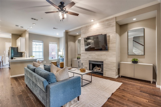 8250 Library St, Frisco, TX 75034 - living area with ceiling fan, crown molding, a tiled fireplace, dark wood-style floors, and baseboards