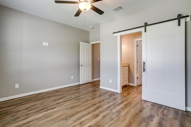 430 Mitchell Blvd, Weatherford, TX 76087 - unfurnished bedroom with a barn door, light wood-style flooring, baseboards, and a ceiling fan