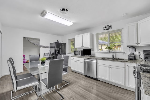 2605 Himes St, Irving, TX 75060 - kitchen with stainless steel appliances, a sink, white cabinetry, light stone countertops, and light wood-style flooring