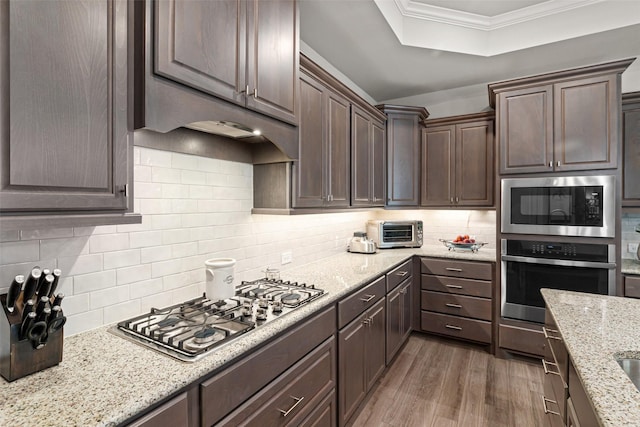 7700 Cerrito Trl, Fort Worth, TX 76123 - kitchen featuring stainless steel appliances, wood finished floors, dark brown cabinets, backsplash, and light stone counters