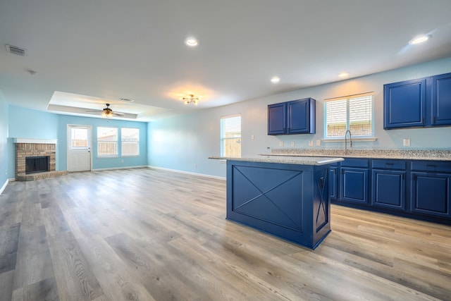 14713 Brandon Dr, Little Elm, TX 75068 - kitchen featuring blue cabinetry, a center island, a ceiling fan, a brick fireplace, and plenty of natural light