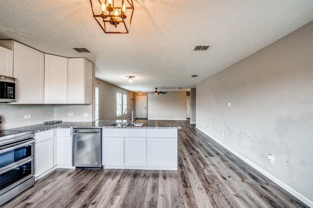 319 Quail Crossing Dr, Sanger, TX 76266 - kitchen with stainless steel appliances, a sink, a peninsula, wood finished floors, and white cabinets