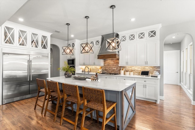 1741 Mountain Creek Ln, Prosper, TX 75078 - kitchen featuring built in appliances, arched walkways, wall chimney range hood, backsplash, and a kitchen breakfast bar